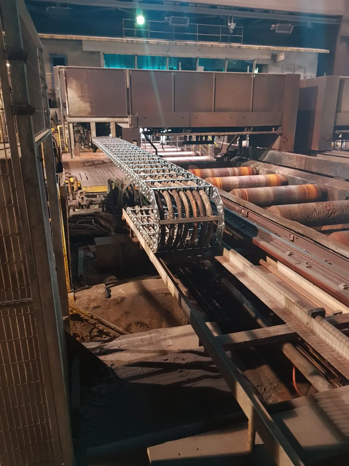 The cable carrier with hoses in the bend, next to the roller conveyor