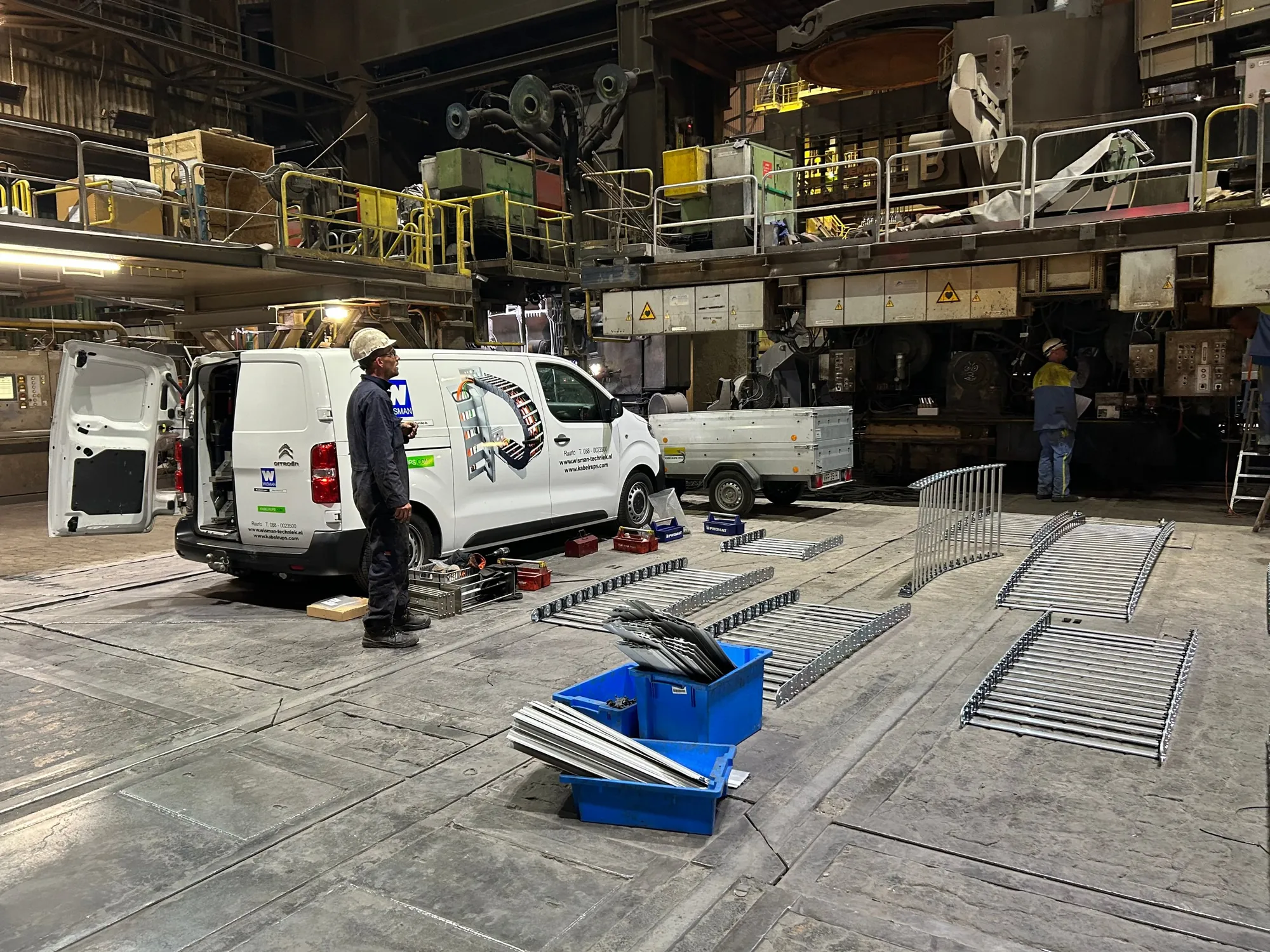 Wisman technician at the van, with the new cable carrier parts laid out in the Tata Steel hall